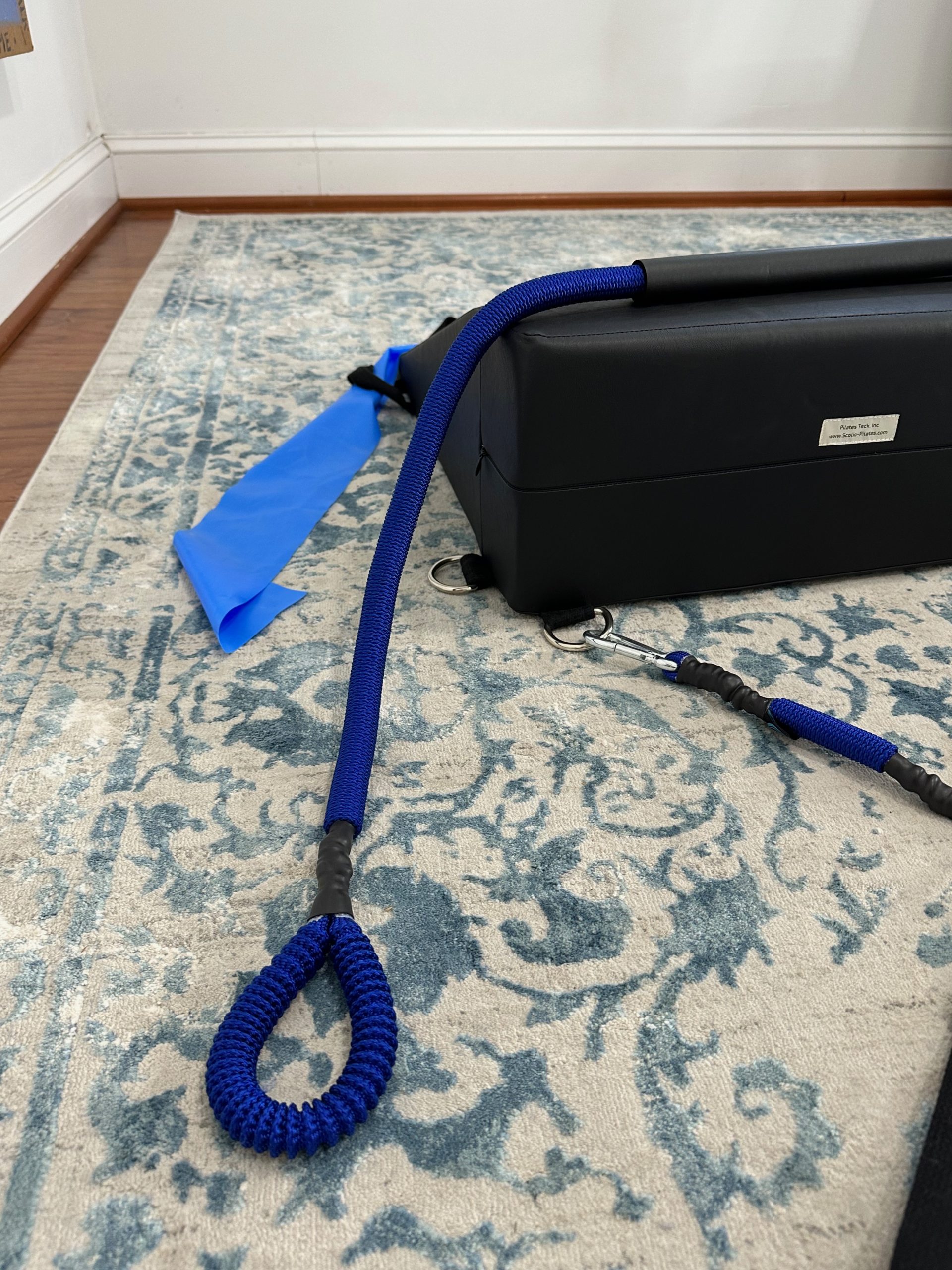 Side view of the K-Fit wedge showing blue resistance cords, carabiner clips, and black fabric handles attached at the base