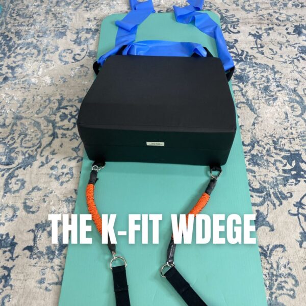 Scolio-PilatesĀ® K-Fit Wedge on a teal mat with blue and orange resistance bands attached, set up for a lengthening and strengthening routine.