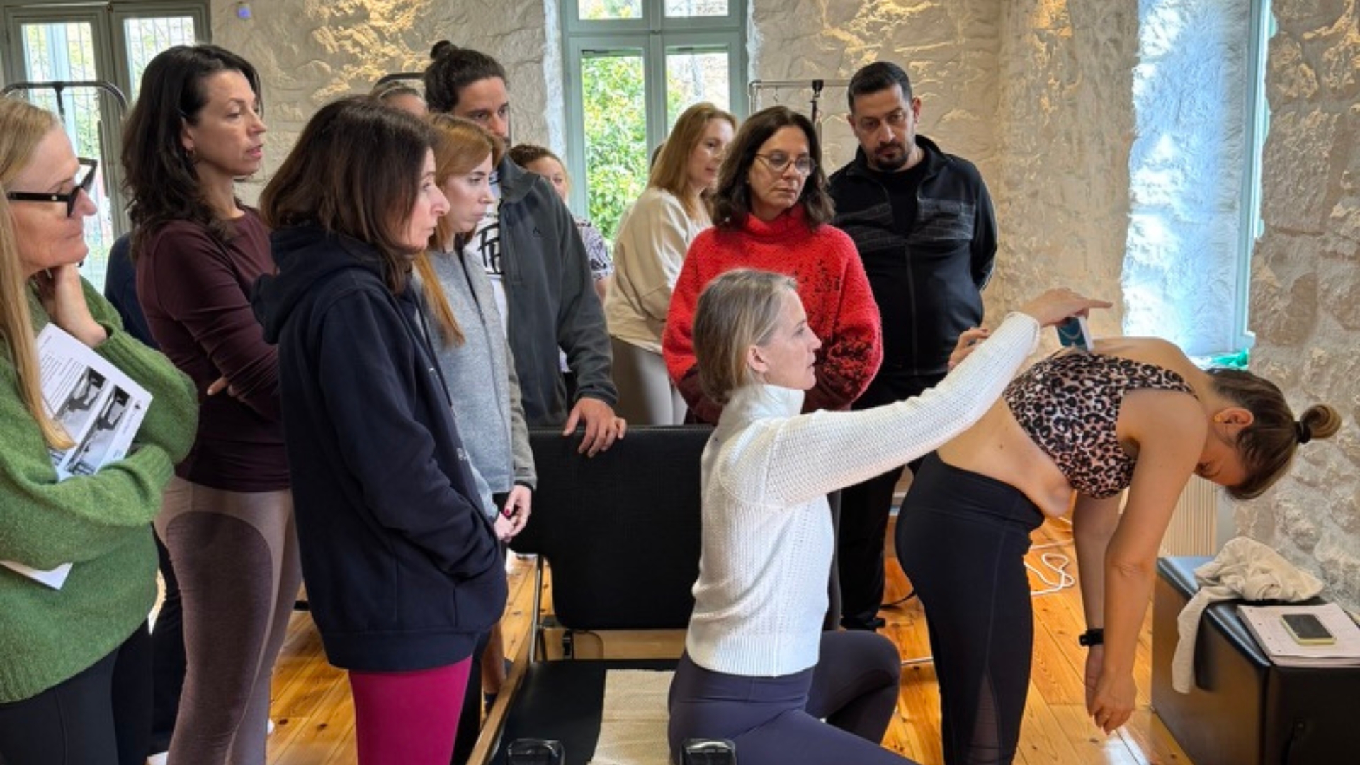 Karena Thek assessing a client's scoliosis curve in a forward bend while Scolio-Pilates training course participants observe