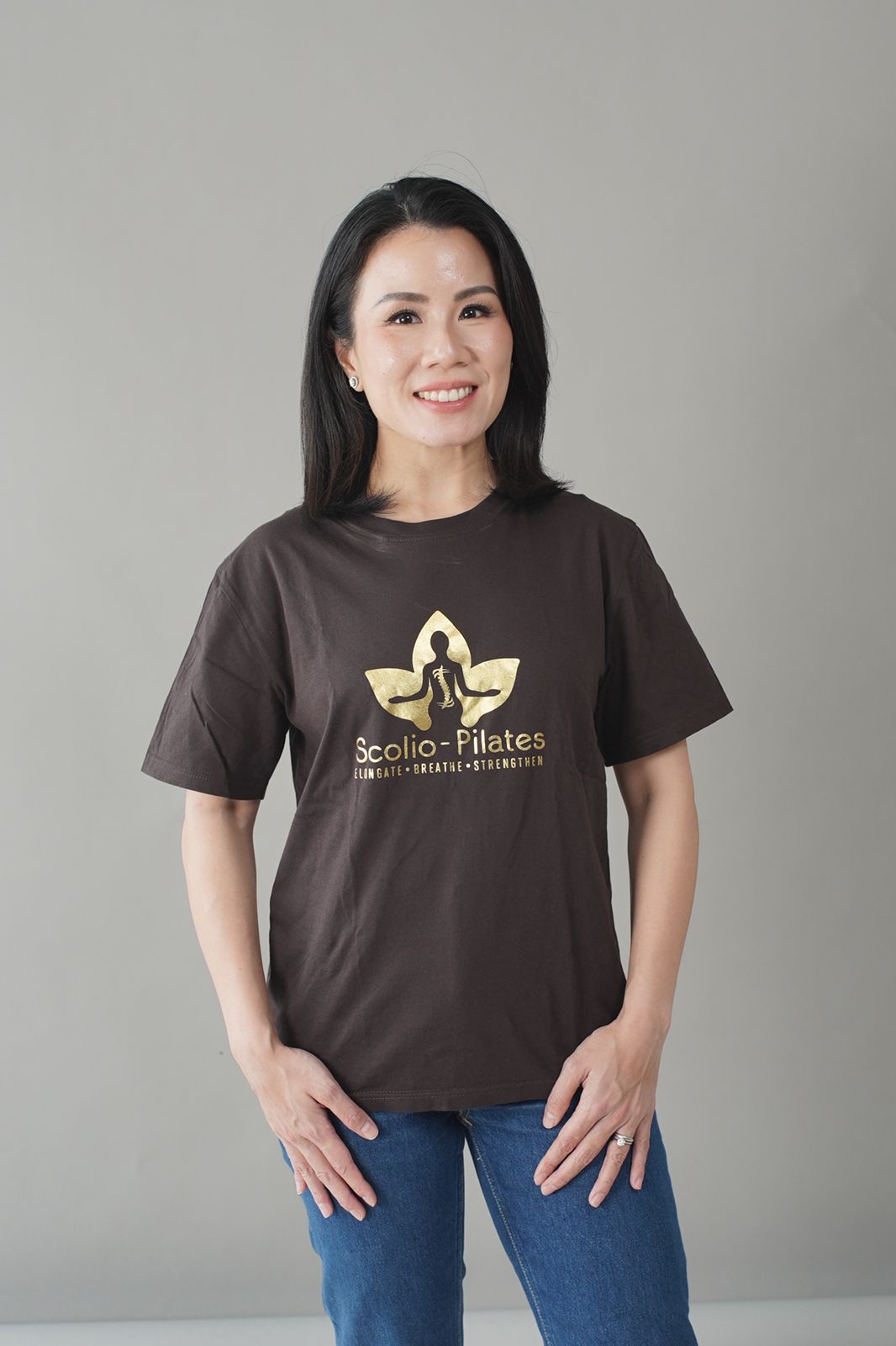 Grace Paliohoetomo, Authorized Scolio-Pilates practitioner in Surabaya, Indonesia, smiling in a Scolio-Pilates shirt and jeans