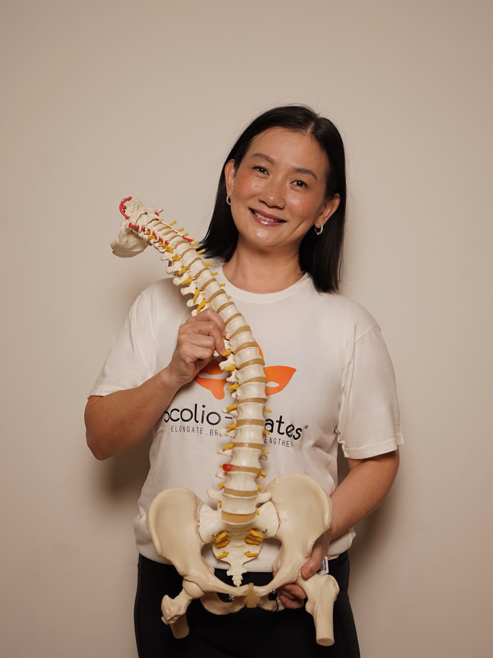 Sansan The, Principal Educator for Scolio-Pilates, holding a spine model in a Scolio-Pilates t-shirt