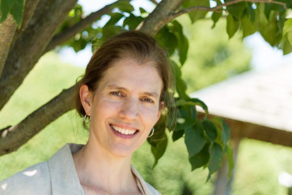 Stasia Siena, Scolio-Pilates practitioner in Champaign, Illinois, smiling outdoors under a tree