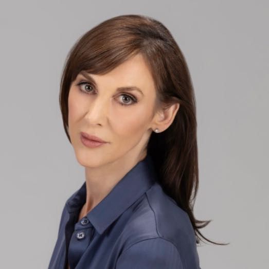 Carey Pickens smiling, wearing a navy blue blouse against a gray background.