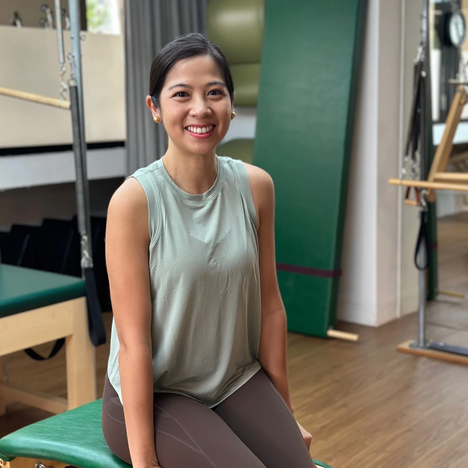 Lisa Dominguez smiling, seated on Pilates equipment in a studio in Singapore.