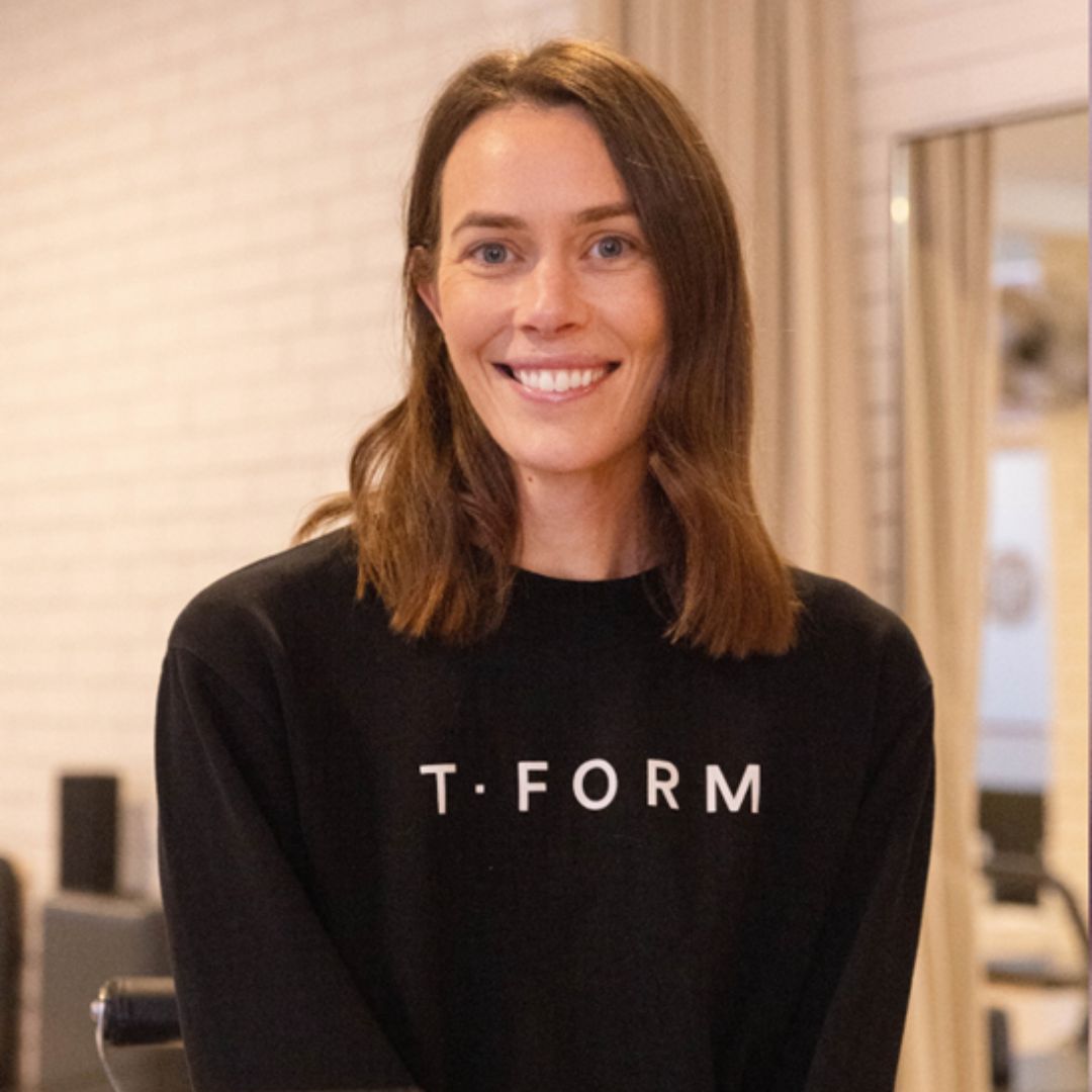 Tamara O'Hare smiling, wearing a black T-Form branded sweatshirt, standing in a bright studio setting.
